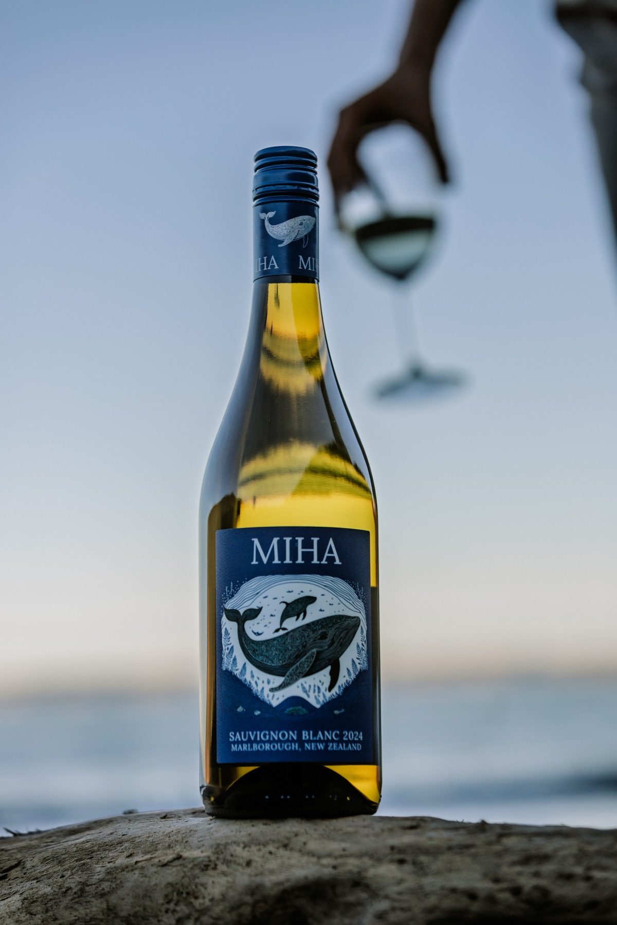 MIHA bottle on driftwood at sunset with a glass behind